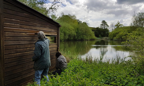 A couple of volunteers painting a bird hide overlooking a pool