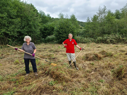 Volunteers Sue and Simon at LCYD in field raking hay after the cut