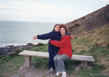 Mother and daughter sitting on a bench with the sea in the background