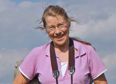 Judi Stretton standing on top of a hill, with her hands in her pockets and binoculars around her neck