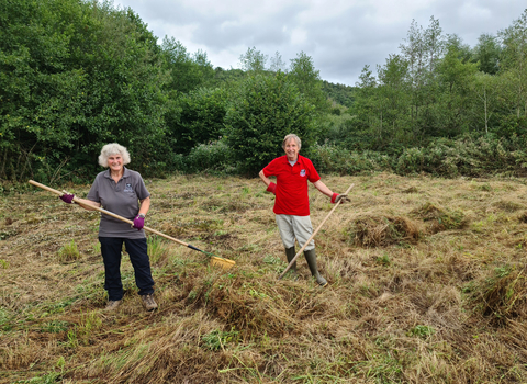Volunteers Sue and Simon at LCYD in field raking hay after the cut