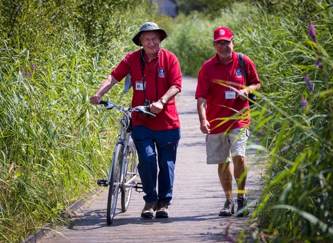 Two volunteers walking down Cors Dyfi Nature Reserve boardwalk, one pushing a bicycle